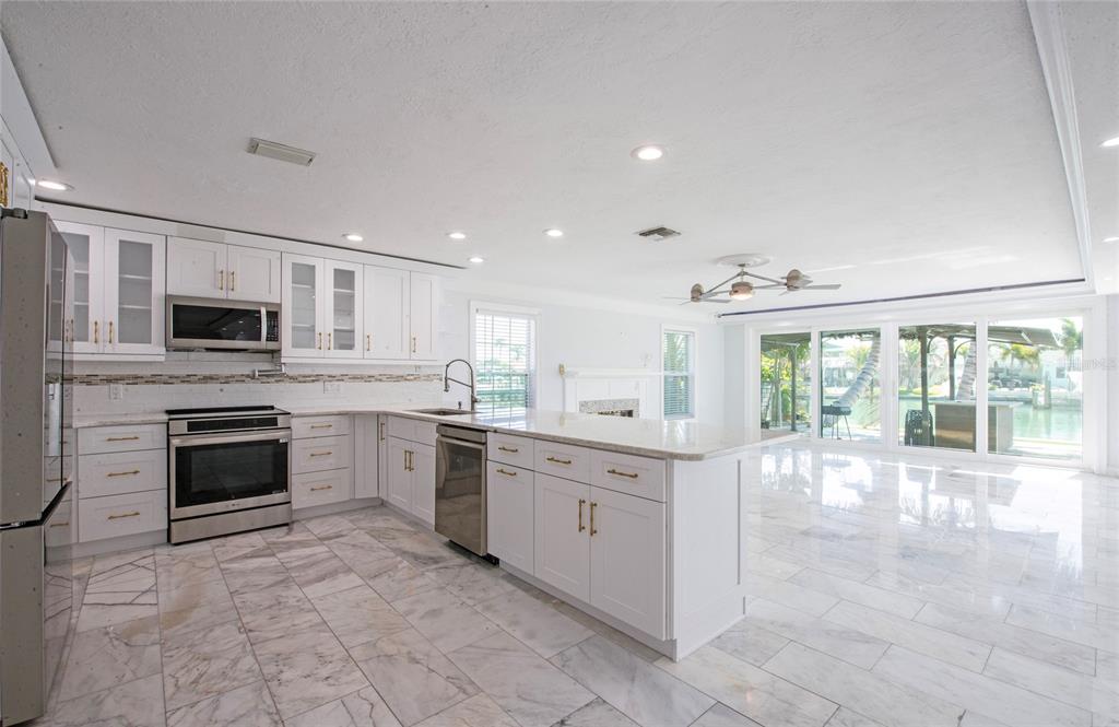 551 Crystal Drive Madeira Beach, FL 33708 - Photo 25 of 46 a large kitchen with stainless steel appliances granite countertop a stove top oven a sink dishwasher a dining table and chairs with wooden floor