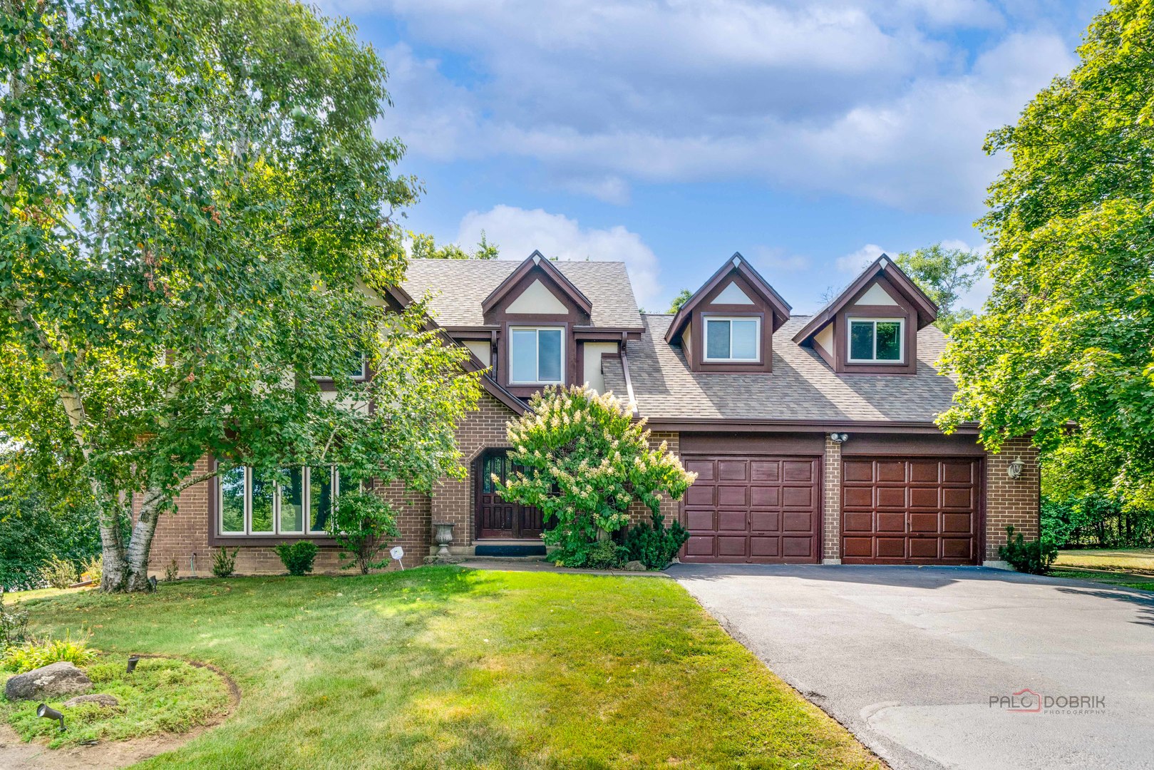 a front view of a house with a garden and trees