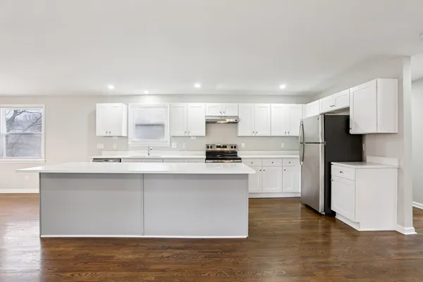 a kitchen with stainless steel appliances granite countertop a stove top oven a sink and white cabinets with wooden floor