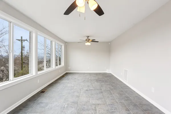 an empty room with chandelier fan and windows