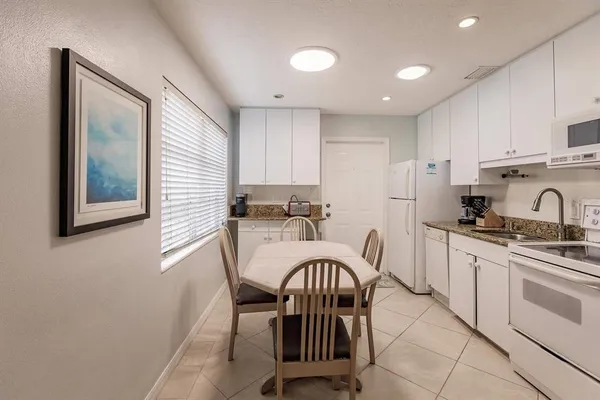 a kitchen with stainless steel appliances granite countertop a stove a sink a refrigerator white cabinets with a dining table and chairs