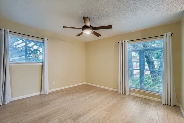 an empty room with wooden floor fan and windows