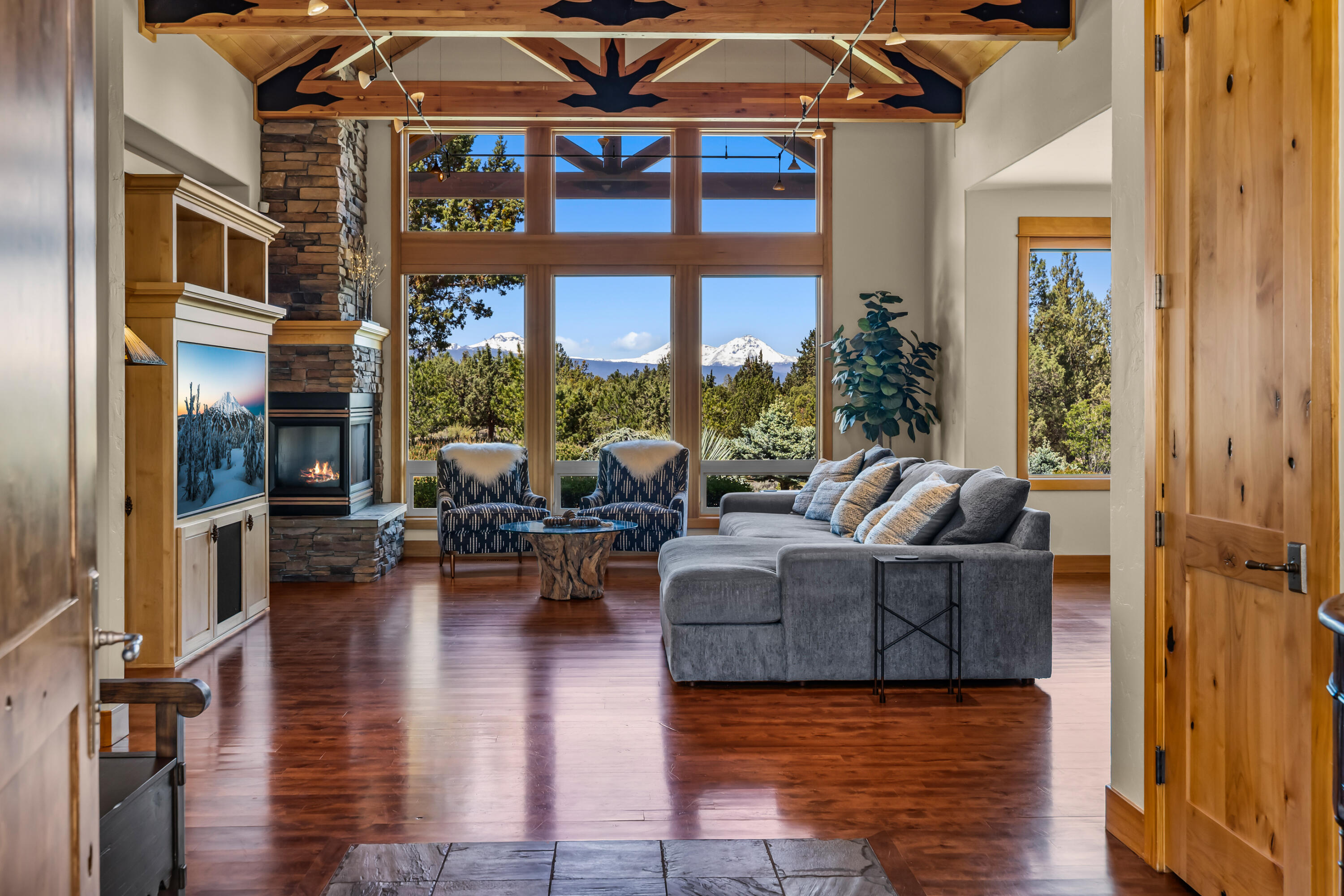 64145 Hunnell Road Bend, OR 97703 - Photo 7 of 65 From the entry, the great room immediately opens to vaulted wood ceilings, real wood floors, stone fireplace detail and walls of glass framing the landscaped grounds and Cascade Mountain views beyond.
