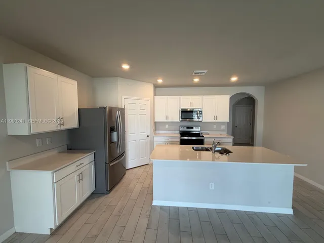 a large kitchen with stainless steel appliances a large counter top a stove a refrigerator white cabinets with wooden floors and floors