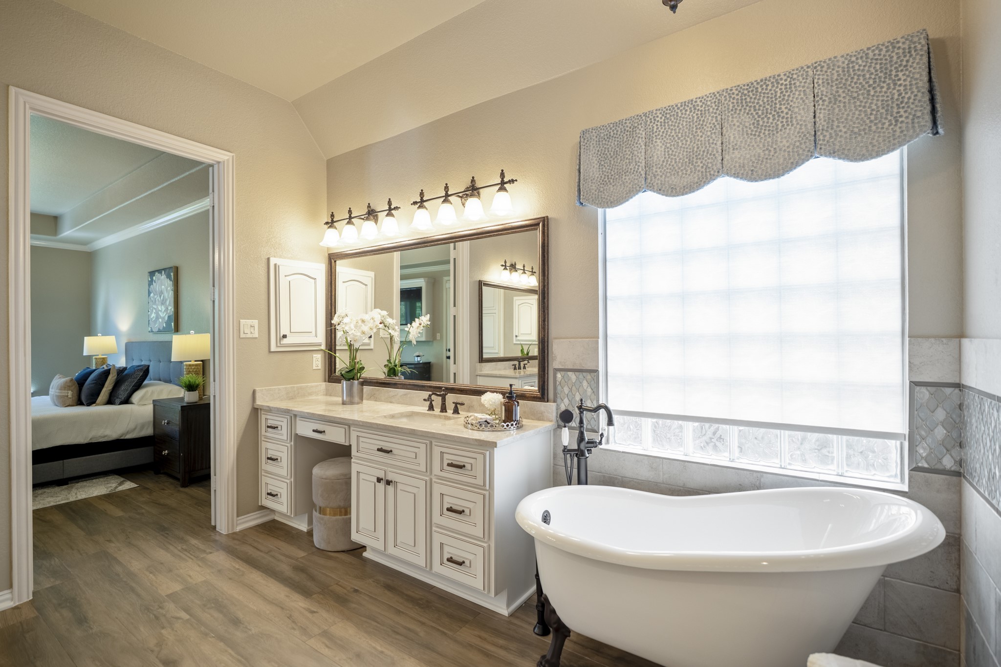 2407 Hendricks Lakes Drive Spring, TX 77388 - Photo 24 of 50 Beside the window, the freestanding clawfoot tub gives the remodeled primary bath a quiet, elevated moment within the suite. Taj Mahal quartzite, custom framed mirrors, upgraded lighting, oil-rubbed bronze fixtures, and the drapery treatment around the tub all add to the finished feel, while the opening on the left leads back into the primary bedroom.