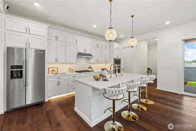 a kitchen with stainless steel appliances granite countertop a sink a stove a refrigerator cabinets and wooden floor