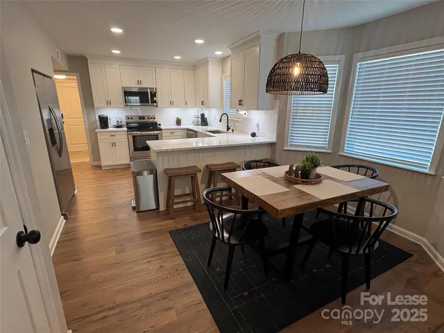 a kitchen with stainless steel appliances kitchen island granite countertop a stove a refrigerator a sink a dining table and chairs with wooden floor