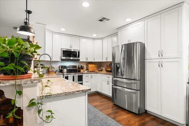 a kitchen with granite countertop a refrigerator a sink a stove and wooden floor