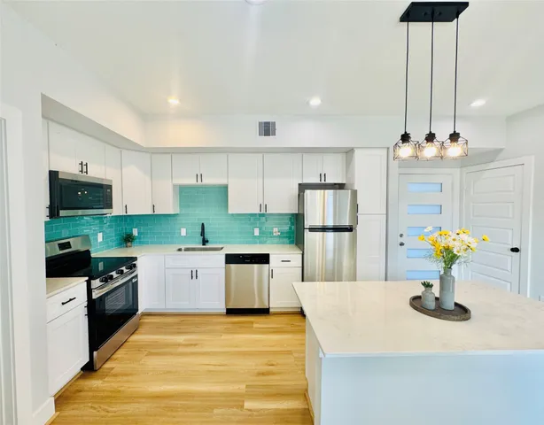 a kitchen with stainless steel appliances kitchen island granite countertop a refrigerator a stove top oven a sink dishwasher and white cabinets with wooden floor