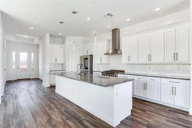 a large kitchen with stainless steel appliances granite countertop a stove a sink and white cabinets with wooden floors