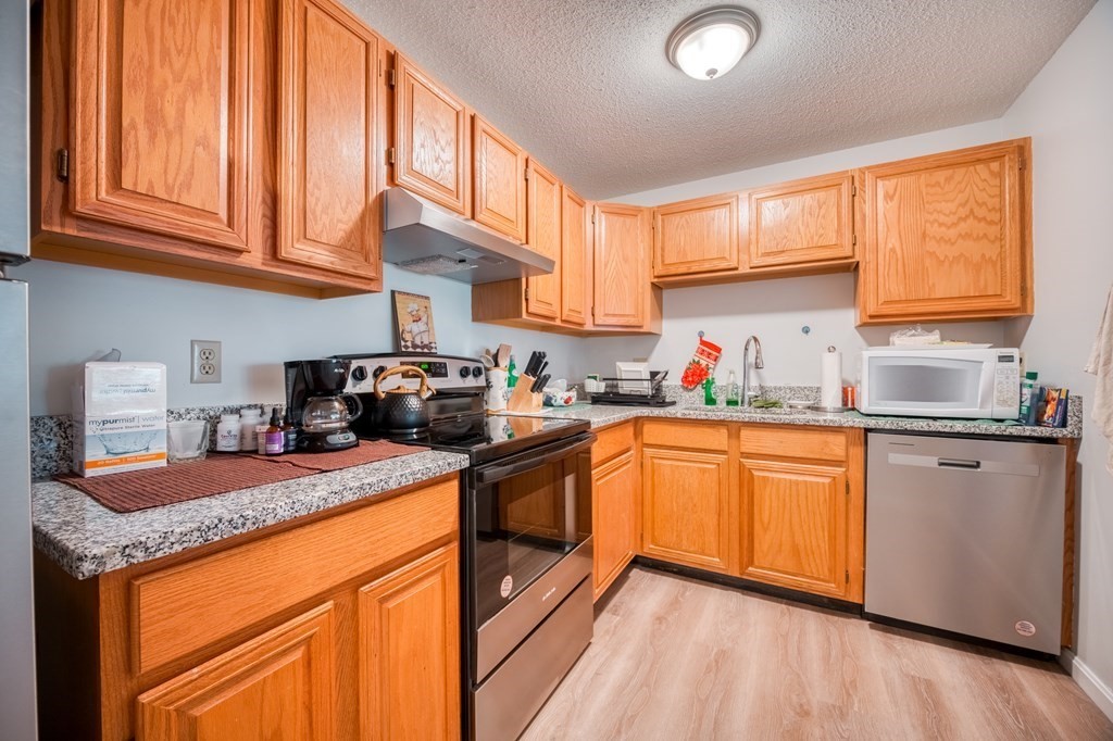 38 Dunham Road, Unit 108 Beverly, MA 01915 - Photo 10 of 30 a kitchen with granite countertop stainless steel appliances a sink dishwasher and cabinets with wooden floor