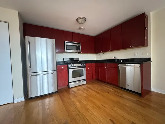 a kitchen with stainless steel appliances granite countertop a refrigerator stove a sink dishwasher and wooden cabinets with wooden floor