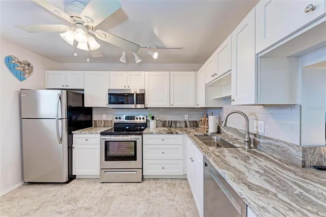 a kitchen with stainless steel appliances granite countertop a stove a sink dishwasher a refrigerator and white cabinets with wooden floor