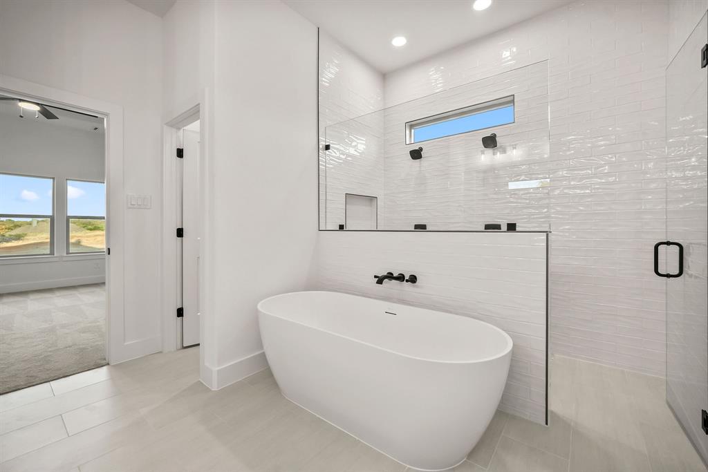 8017 Rnch Vw Place Springtown, TX 76082 - Photo 13 of 18 Freestanding soaking tub with matte black fixtures, walk-in shower with glass enclosure, tiled shower walls with horizontal accent window, and light-toned tile flooring