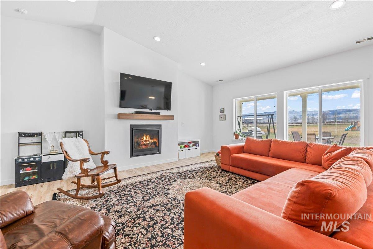 8843 Highway 78 Marsing, ID 83639 - Photo 14 of 48 Living room featuring a glass covered fireplace, vaulted ceiling, wood finished floors, and recessed lighting