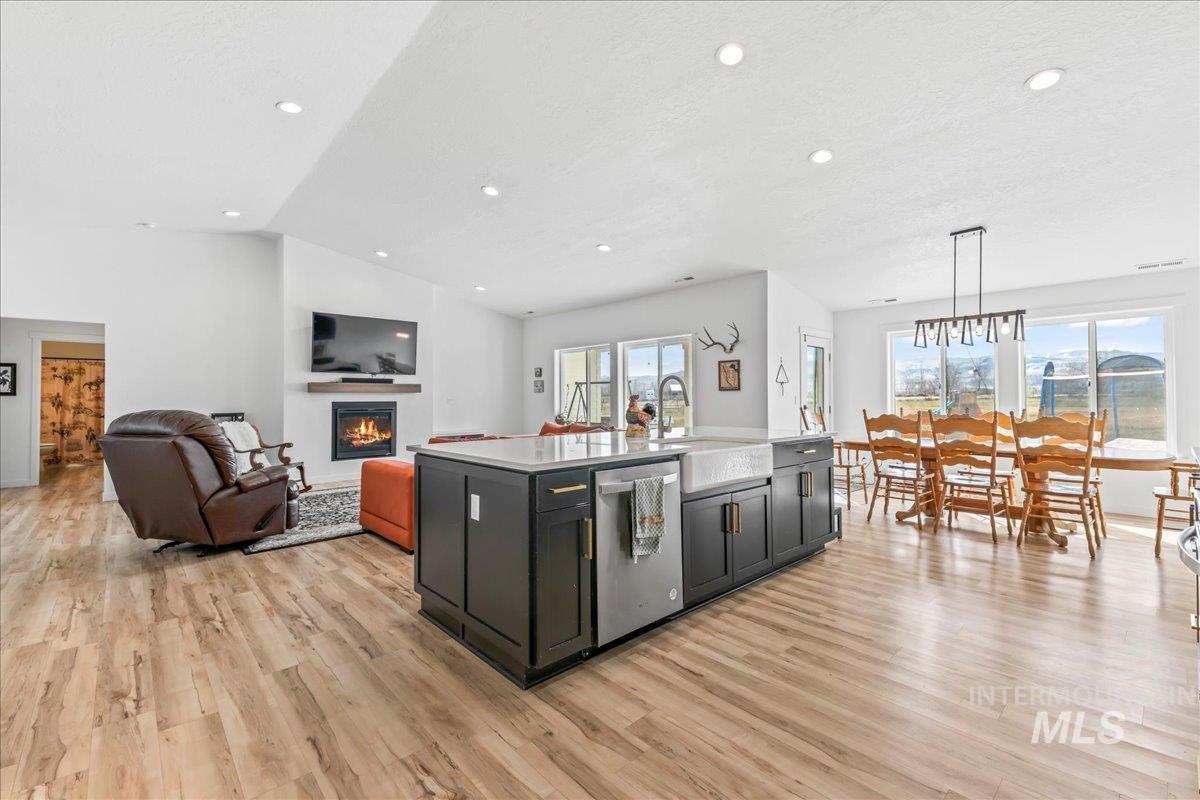 8843 Highway 78 Marsing, ID 83639 - Photo 47 of 48 Kitchen with open floor plan, a center island with sink, a glass covered fireplace, light wood-style flooring, and dishwasher