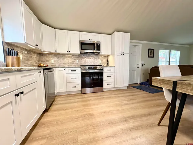 a kitchen with stainless steel appliances granite countertop a refrigerator a stove top oven a sink dishwasher and white cabinets with wooden floor