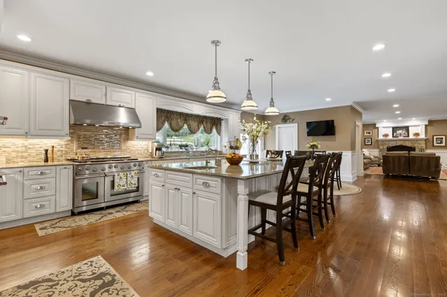 a kitchen with stainless steel appliances kitchen island granite countertop a stove a sink a oven a dining table and chairs with wooden floor