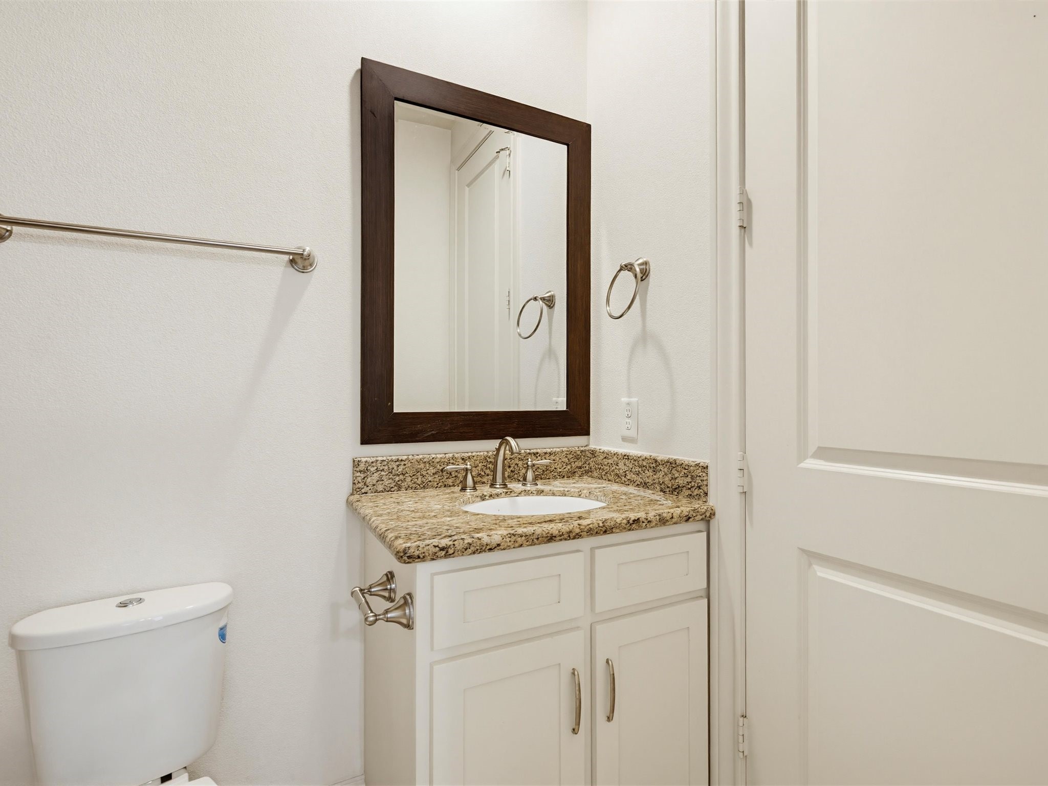 9427 London Bridge Station Houston, TX 77045 - Photo 18 of 30 Compact bathroom with a granite countertop, under-mount sink, and a large framed mirror. Features include a toilet, towel bar, and neutral-toned cabinetry.