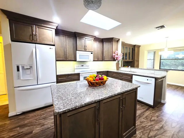 a large kitchen with stainless steel appliances granite countertop a refrigerator a sink dishwasher a stove and white countertops with wooden floor