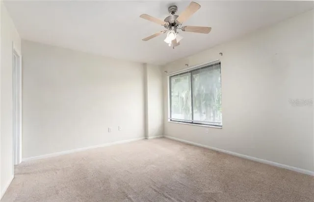 an empty room with a chandelier fan and windows