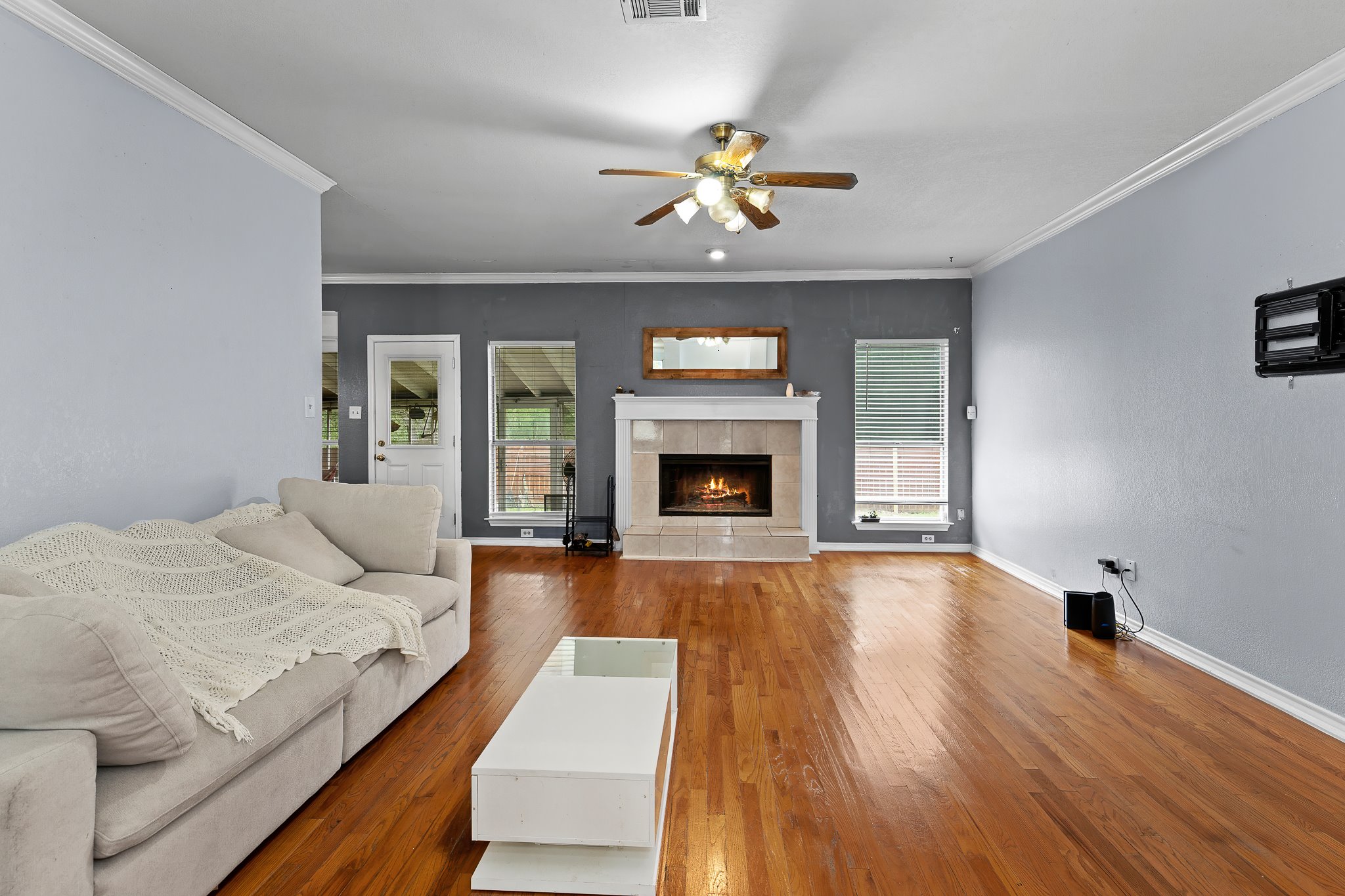 11737 Rydalwater Lane Austin, TX 78754 - Photo 12 of 40 Living area featuring polished wood-finish flooring, a ceiling fan with integrated lighting, and a fireplace with a stone surround and mantel