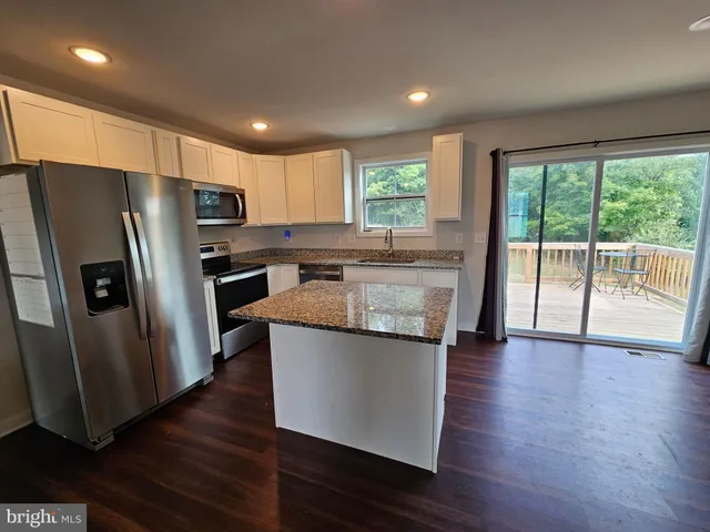 a kitchen with stainless steel appliances granite countertop a refrigerator a sink a stove a microwave and island with wooden floor