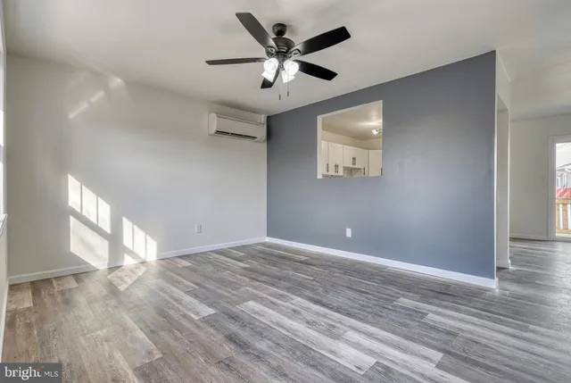 a view of an empty room with wooden floor and a ceiling fan