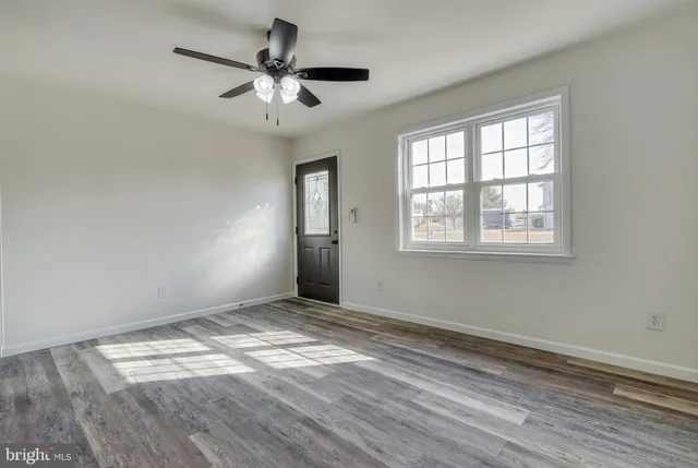 an empty room with wooden floor chandelier fan and windows
