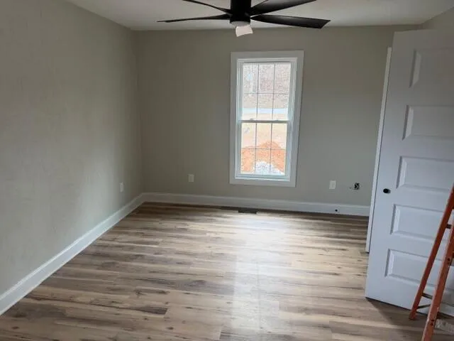 an empty room with wooden floor fan and windows
