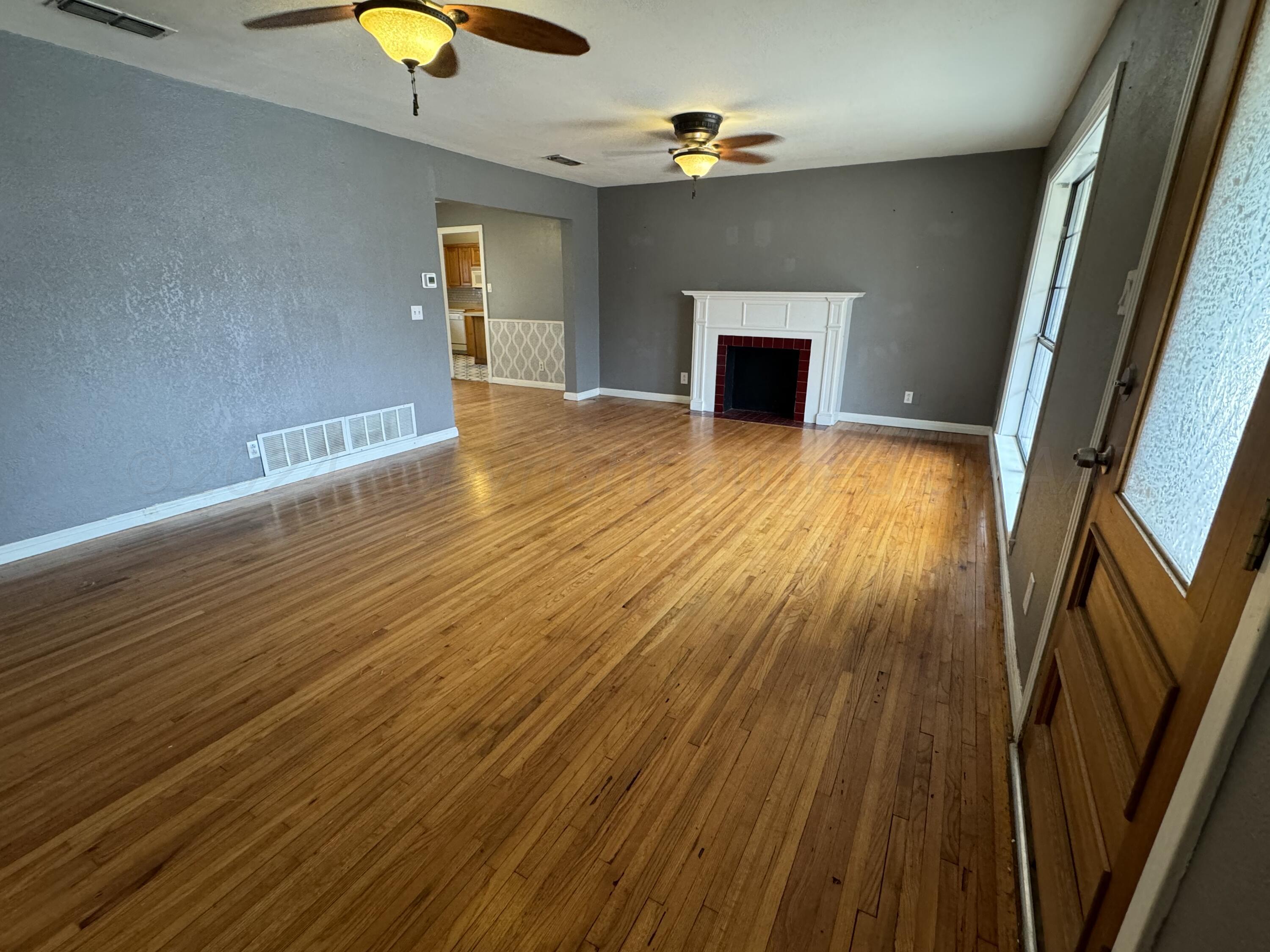 a view of an empty room with wooden floor fireplace and a window