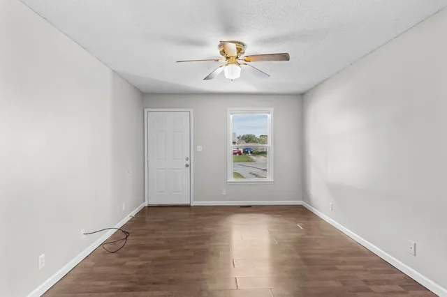 an empty room with wooden floor fan and windows