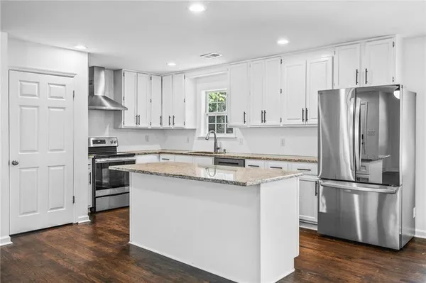 a kitchen with stainless steel appliances granite countertop a refrigerator a stove a sink and white cabinets with wooden floor
