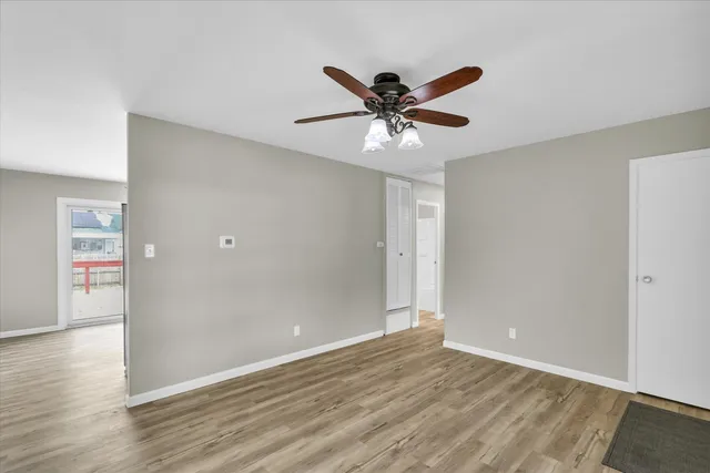 a view of an empty room with wooden floor and a ceiling fan