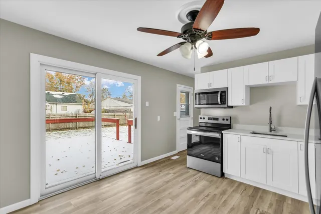 a kitchen with stainless steel appliances granite countertop a stove top oven a sink a refrigerator with white cabinets and wooden floor