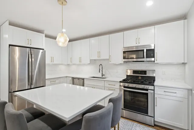 a kitchen with stainless steel appliances a stove a sink a microwave a refrigerator a stove a white table and chairs