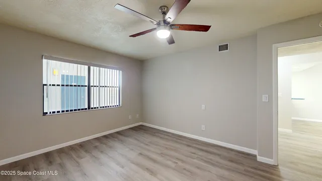 an empty room with wooden floor chandelier fan and windows