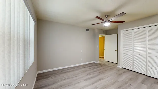 an empty room with wooden floor fan and windows
