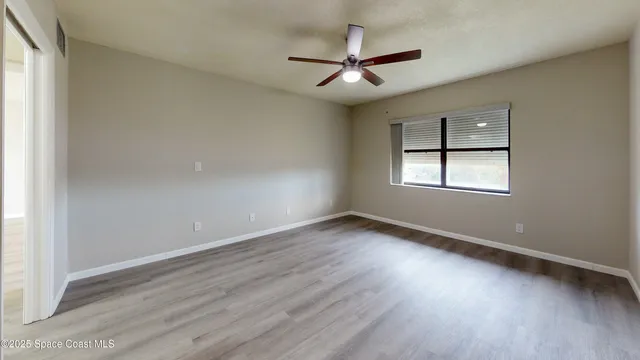 an empty room with wooden floor ceiling fan and windows