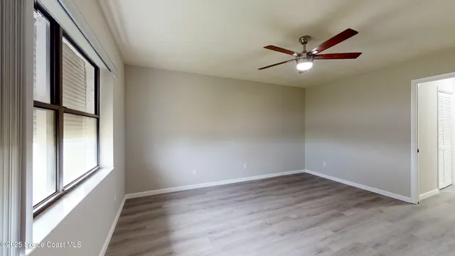 an empty room with wooden floor fan and windows