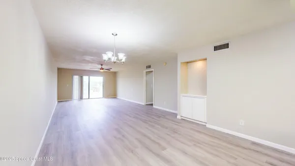 an empty room with wooden floor chandelier fan and windows