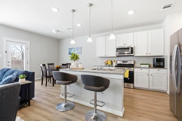 a kitchen with stainless steel appliances granite countertop a refrigerator a stove a sink a dining table and chairs with wooden floor
