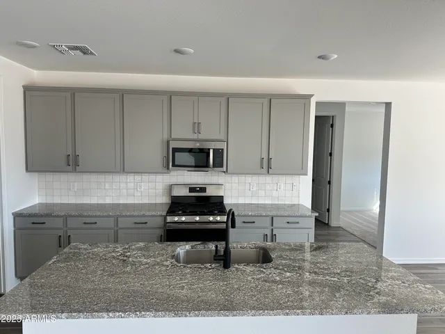 a kitchen with stainless steel appliances kitchen island granite countertop a stove a sink and a white cabinets