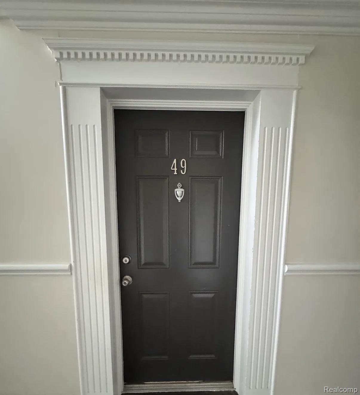 2247 Walton Blvd. Rochester, MI 48309 - Photo 1 of 12 Panel door with ornate door knocker and number 49, framed by decorative fluted trim and a dentil crown molding