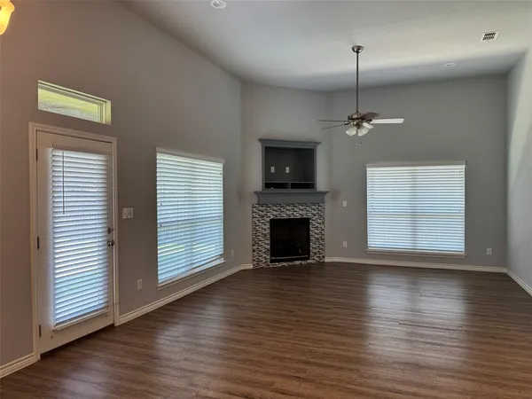 an empty room with wooden floor fireplace and windows