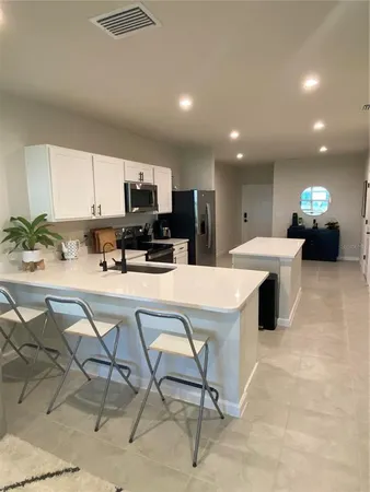 a view of kitchen with stainless steel appliances kitchen island granite countertop a stove a sink a refrigerator and a dining table with white cabinets