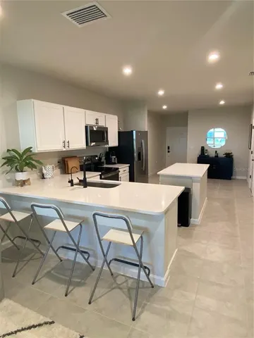 a view of kitchen with stainless steel appliances kitchen island granite countertop a stove a sink a refrigerator and a dining table with white cabinets