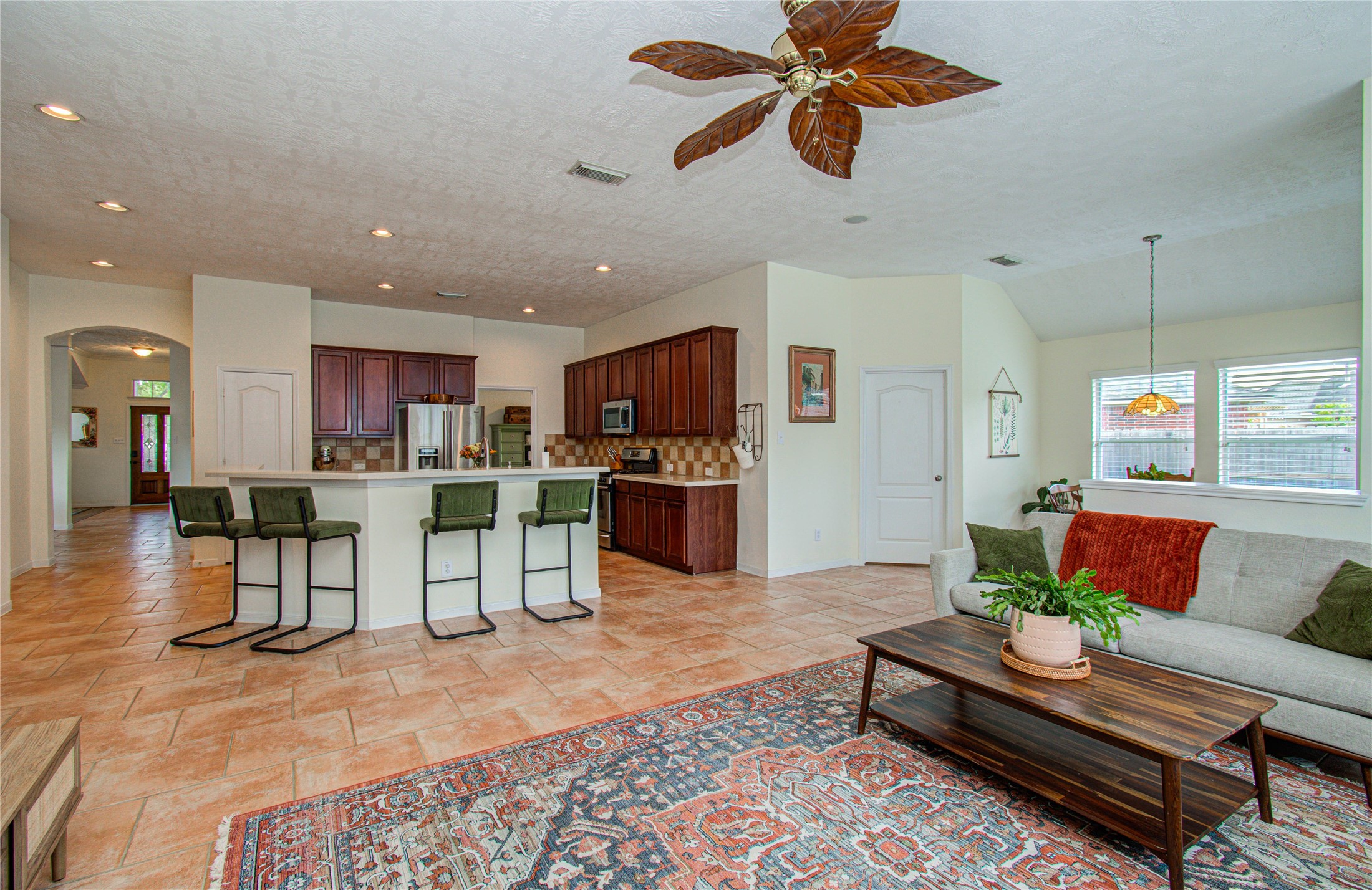 20007 Alcea Court Spring, TX 77379 - Photo 16 of 36 This inviting open-concept living space features a spacious kitchen with a breakfast bar, modern appliances, and warm wood cabinetry. The adjacent living area is bright, with large windows and a ceiling fan, complemented by a cozy seating area and attractive tile flooring. Perfect for entertaining and family gatherings.
