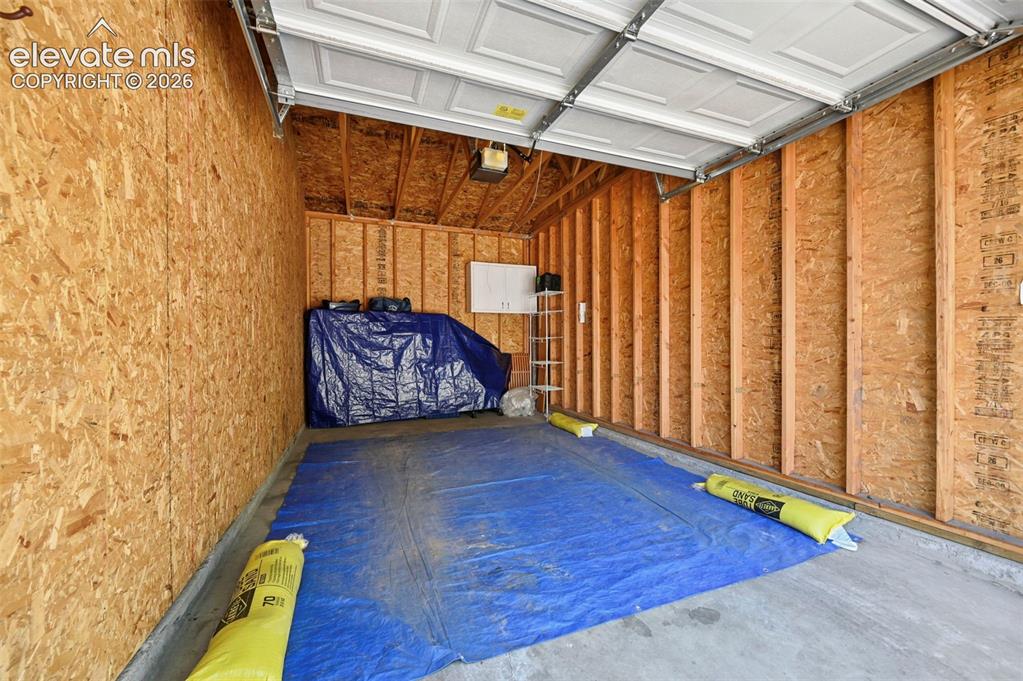 3715 Riviera Grove, Unit 101 Colorado Springs, CO 80922 - Photo 35 of 36 Spacious garage featuring a concrete floor, exposed wood framing, and an overhead garage door