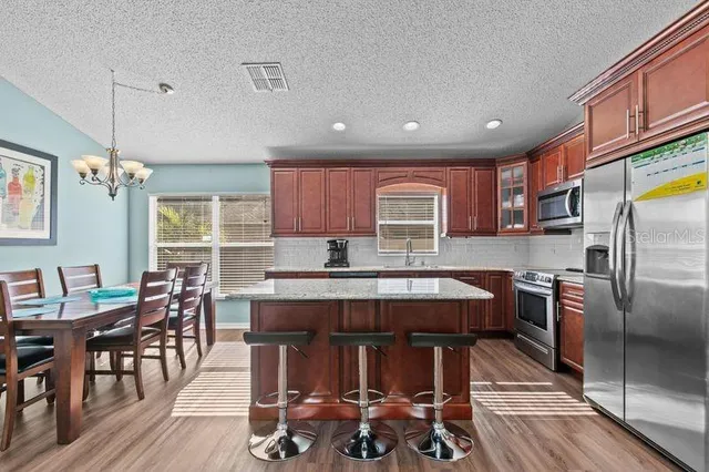 a kitchen with stainless steel appliances granite countertop a table chairs sink refrigerator and microwave